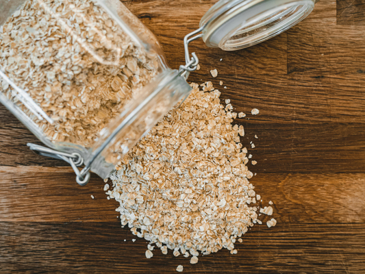 un bocal en verre rempli de flocons d'avoine qui déborde sur une planche en bois brut
